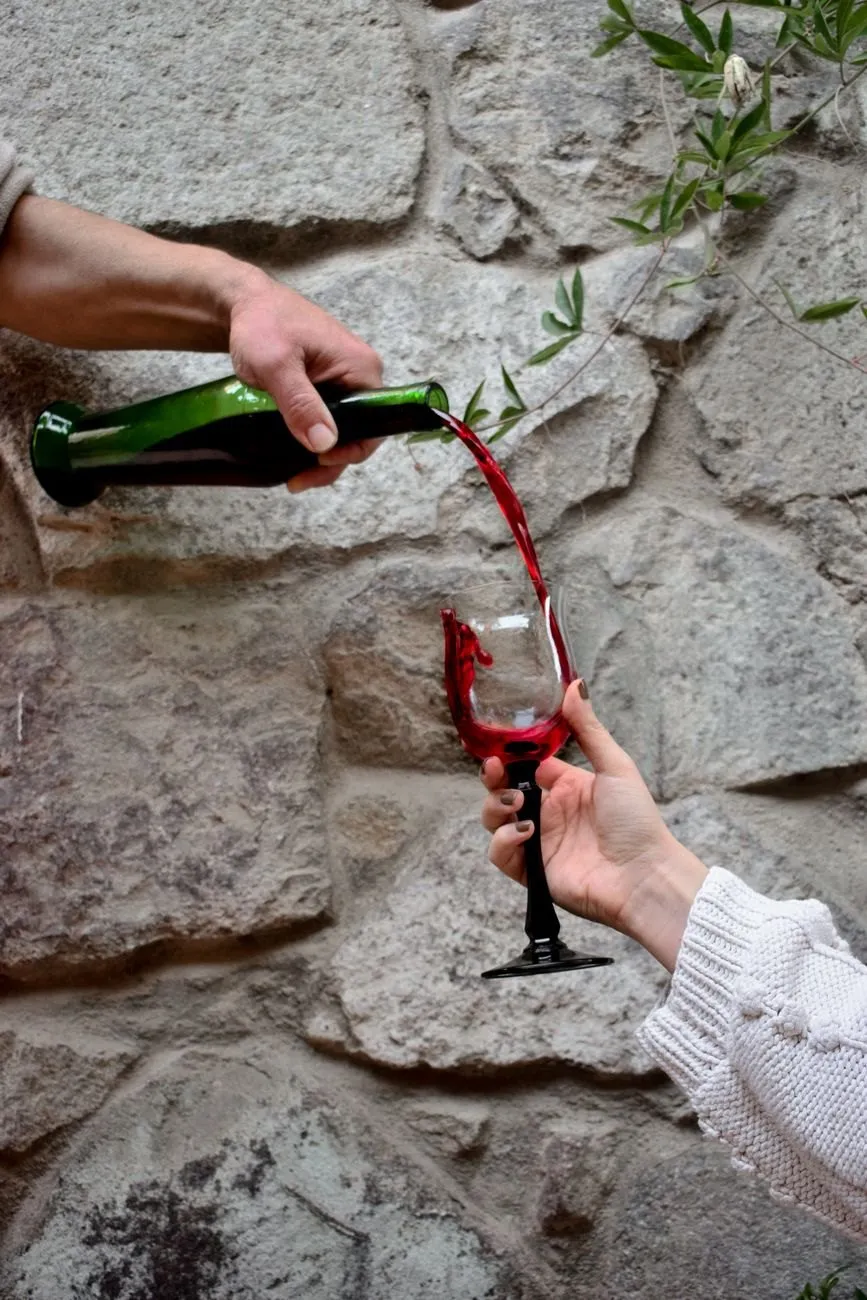 Red wine being poured from a green unlabelled bottle into a glass against a stone wall